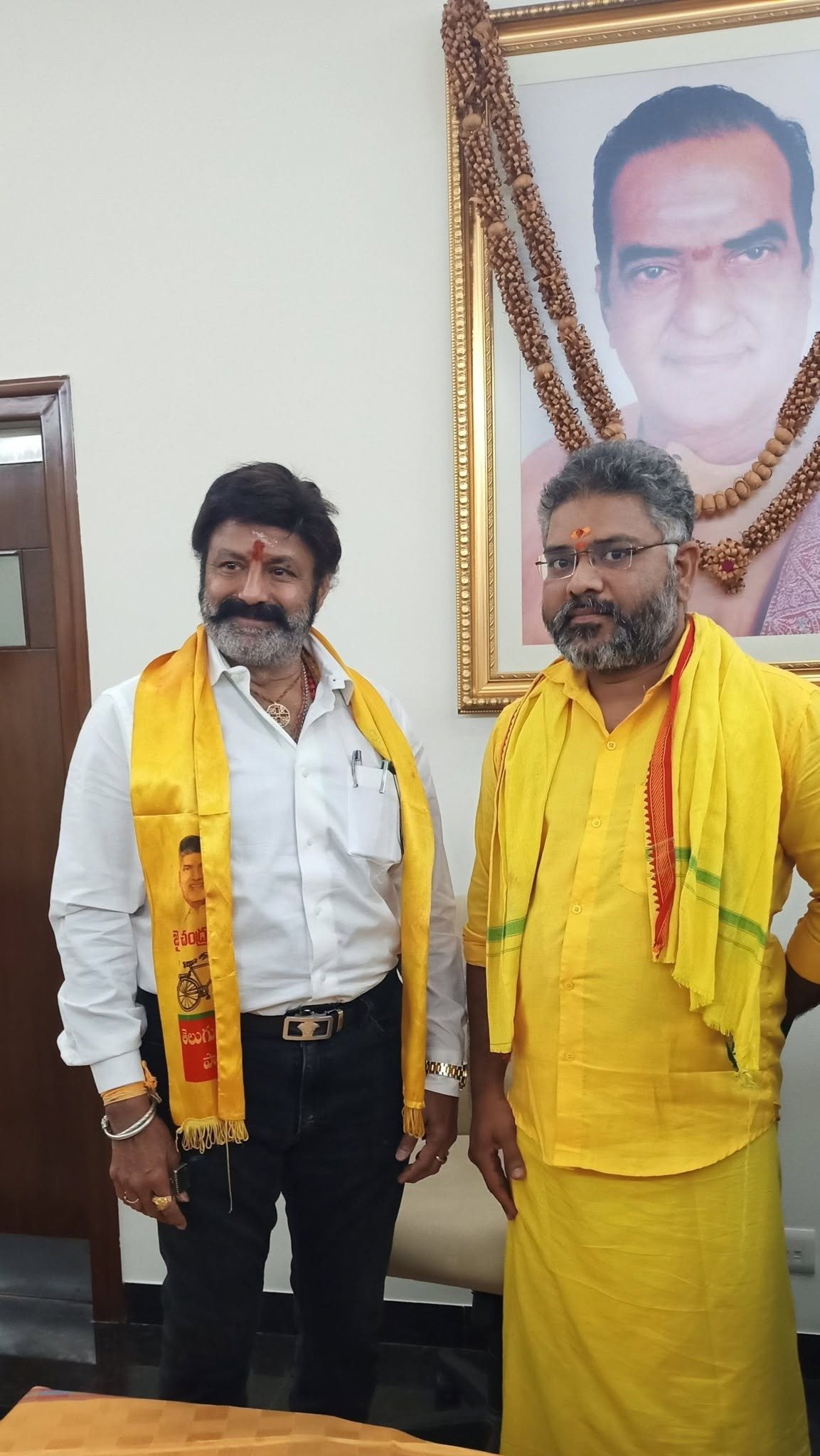 Talikota Hari Krishna with Nandamuri Balakrishna, Hindupur MLA, beneath a portrait of N.T. Rama Rao